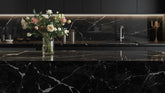 Modern kitchen with a sleek black Wilsonart countertop and backsplash, featuring marble-style veining and a floral arrangement on the island.