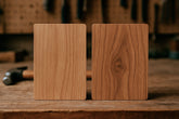 Two high pressure laminates wood samples on a rustic workbench; the left sample has a lighter wood grain, while the right is darker with a visible knot, set against a blurred background of workshop tools.